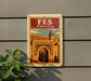 a vintage-style poster of the Fes medina in Morocco, with a large archway and a tower in the background.
