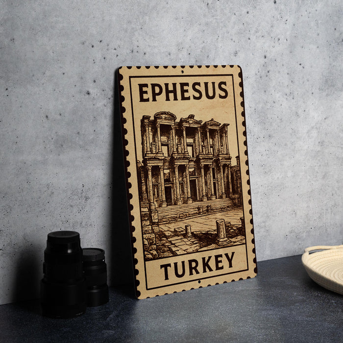 A wooden sign with an illustration of an ancient building, labeled "Ephesus Turkey", is displayed on a table next to some black camera lenses.
