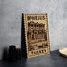 A wooden sign with an illustration of an ancient building, labeled "Ephesus Turkey", is displayed on a table next to some black camera lenses.