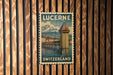 A vintage postage stamp from Switzerland featuring a tower and a bridge, mounted on a wooden wall.