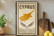 a decorative sign with the word "CYPRUS" on it, along with a map of the island of Cyprus. The sign is placed on a shelf next to a wooden cutting board and some potted plants.