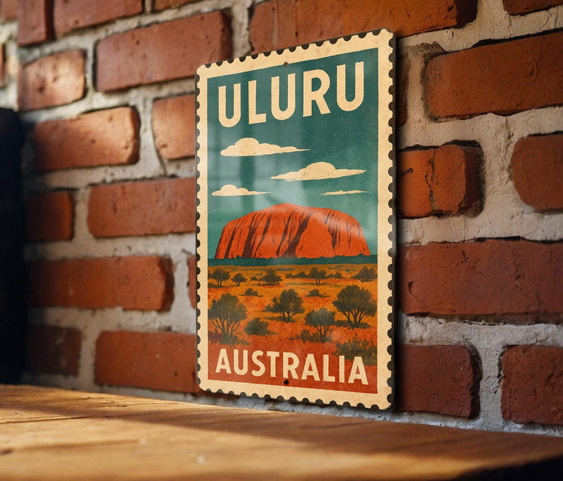 A vintage-style stamp depicting Uluru, a famous rock formation in Australia, is displayed on a brick wall.