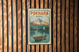 A vintage-style metal sign with the text "POKHARA NEAL" and an illustration of a mountain landscape with a boat on a lake.