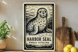 A metal sign featuring a black and white illustration of a seal, with the text "HARBOR SEAL PHOCA VITULINA" below it.