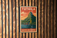 A vintage-style metal sign with the text "TUTUILA AMERICAN SAMOA" displayed on a wooden wall.