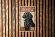 A flat-coated retriever dog is depicted on a postage stamp-like sign, which is mounted on a wooden wall.