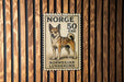A postage stamp featuring a dog, specifically a Norwegian Lundehund, is displayed on a wooden wall.