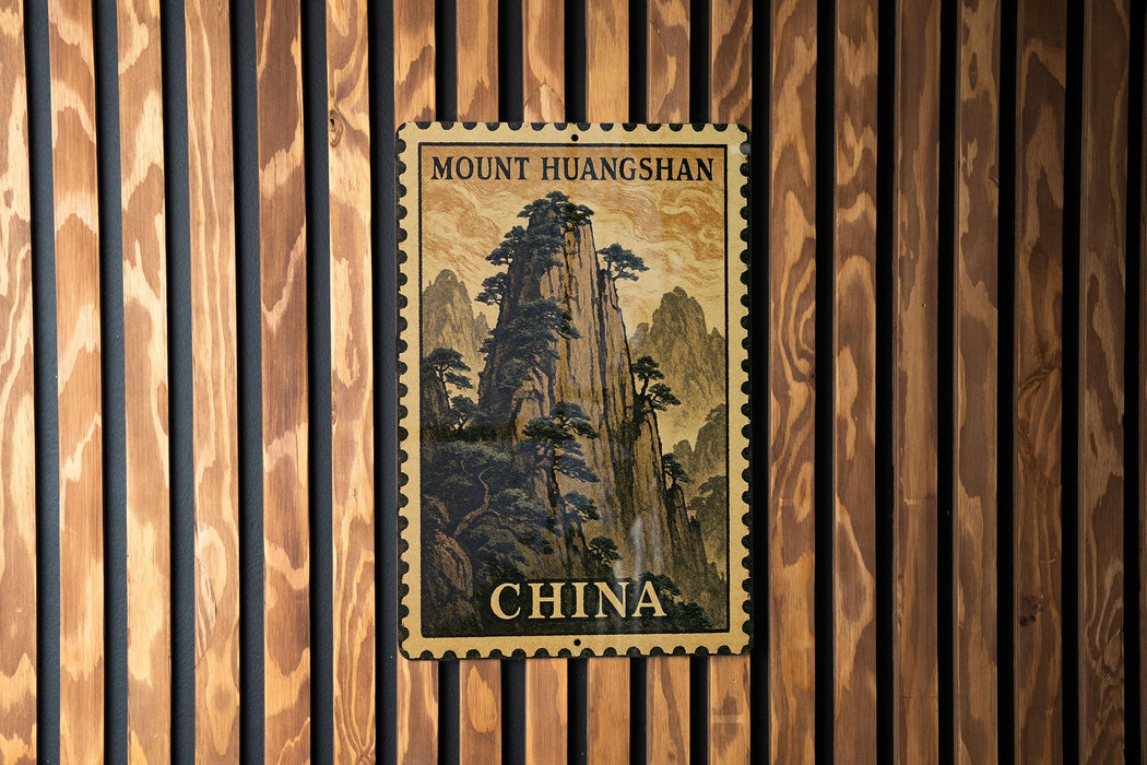 A framed postcard featuring a mountainous landscape with trees, mounted on a wooden wall.