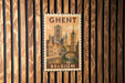 A vintage postage stamp from Belgium featuring a cityscape with a castle and a bridge, mounted on a wooden wall.
