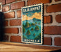 A vintage postage stamp depicting a tropical island landscape with palm trees and water, hanging on a brick wall.