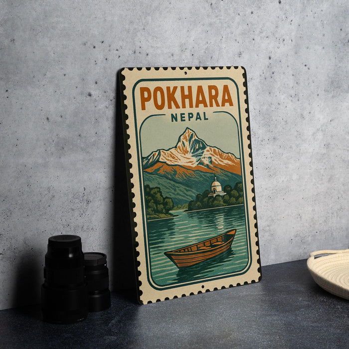 A vintage-style metal sign with a mountain landscape and a boat, depicting the Pokhara region in Nepal.