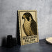 A framed poster of a peregrine falcon is displayed on a wall, with a stack of black camera lenses and a white dish visible to the side.