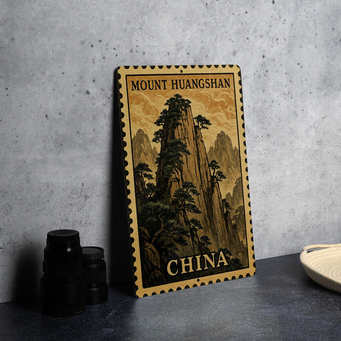 A framed postcard depicting a mountainous landscape with trees, placed on a table next to some black camera lenses.