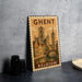 A vintage-style metal sign with the text "Ghent" and "Belgium" printed on it, featuring an illustration of a cityscape with a castle and a bridge.