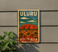 A vintage-style sign with the text "ULURU AUSTRALIA" and an illustration of Uluru, a large red rock formation in the Australian outback, is displayed on a wall.
