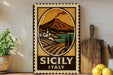 A vintage-style metal sign with a landscape depicting a village and a mountain, along with the text "SICILY ITALY". The sign is displayed on a shelf next to a wooden cutting board and a potted plant.