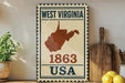 A vintage-style metal sign with the text "WEST VIRGINIA 1863 USA" displayed on it, along with a map of the state of West Virginia. The sign is placed on a wooden surface, with a potted plant, a wooden cutting board, and some lemons nearby.