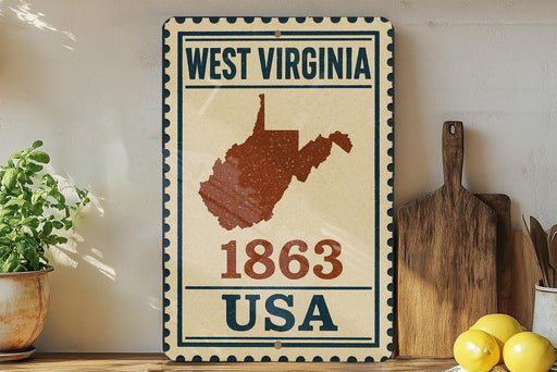 A vintage-style metal sign with the text "WEST VIRGINIA 1863 USA" displayed on it, along with a map of the state of West Virginia. The sign is placed on a wooden surface, with a potted plant, a wooden cutting board, and some lemons nearby.