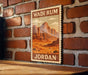 A vintage-style poster of a desert landscape with mountains and a desert scene, mounted on a brick wall.