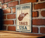A vintage-style sign displaying the state of West Virginia and the year 1863, mounted on a brick wall.