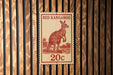 A red kangaroo stamp with the value of 20 cents is displayed on a wooden wall.