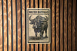 a sign with the word "Water Buffalo" on it, mounted on a wooden wall.