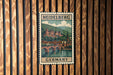 A vintage-style postage stamp from Heidelberg, Germany, featuring a castle and bridge in the background, mounted on a wooden wall.