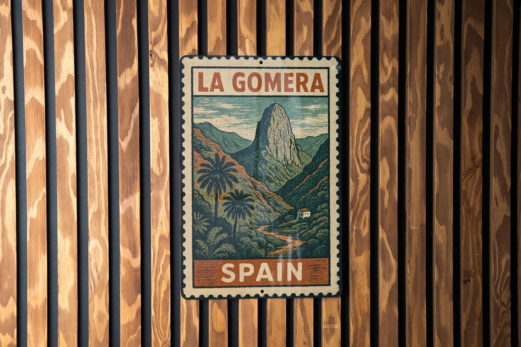 A vintage-style metal sign with the text "LA GOMERA" and "SPAIN" printed on it, hanging on a wooden wall.