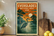 a vintage-style metal sign with a postage stamp design, depicting a serene scene of a bird standing in a body of water with a sunset in the background.
