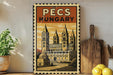 A vintage-style poster of the Pecs Cathedral in Hungary, featuring an illustration of the cathedral's spires and architecture, is displayed on a wall next to kitchen utensils and a potted plant.