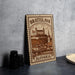A metal sign with the text "BRATISLAVA SLOVAKIA" and an illustration of a castle, placed on a table next to some black camera lenses.