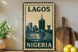 A vintage-style metal sign with the text "LAGOS NIGERIA" displayed prominently, featuring a cityscape illustration. The sign is placed on a shelf next to a wooden cutting board and a potted plant.
