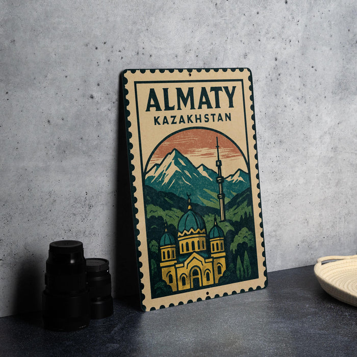 A metal sign with a mountain landscape and a building, likely representing the Almaty region in Kazakhstan, is displayed on a table.