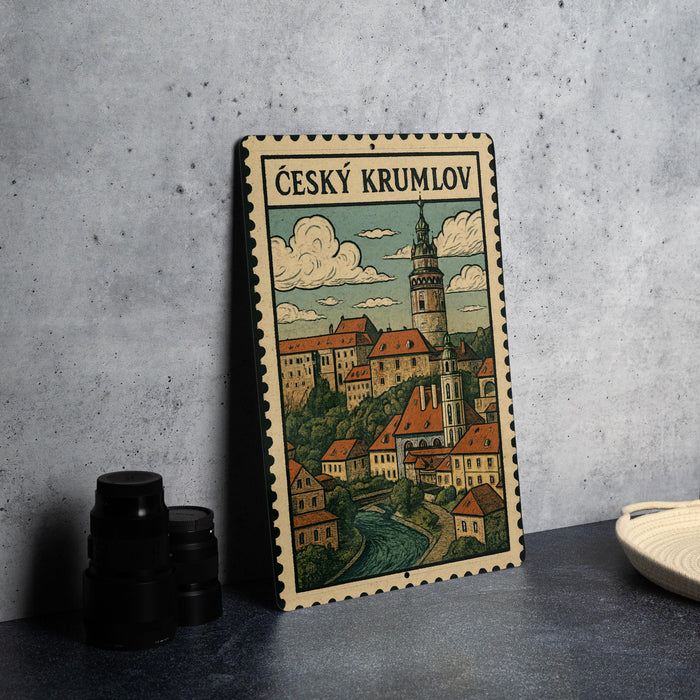 A metal sign with a vintage illustration of a town, featuring a castle, buildings, and a river, is displayed on a table.