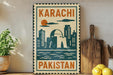 A vintage-style sign with the text "KARACHI PAKISTAN" displayed on a wall, with a cityscape illustration below it. The sign is surrounded by various kitchen utensils and a potted plant, creating a homely atmosphere.
