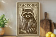 a raccoon illustration on a wooden sign, placed on a shelf next to a potted plant and a wooden cutting board.