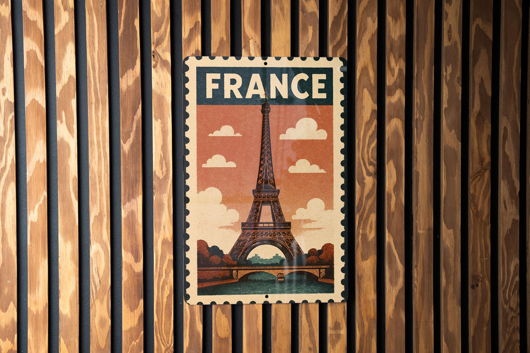 A vintage-style metal sign with the word "FRANCE" prominently displayed, featuring an illustration of the Eiffel Tower against a cloudy sky.