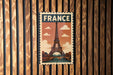 A vintage-style metal sign with the word "FRANCE" prominently displayed, featuring an illustration of the Eiffel Tower against a cloudy sky.