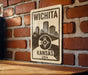 A metal sign displaying the name "WICHITA" and the location "KANSAS USA" is mounted on a brick wall.