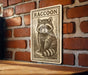 a raccoon on a sign, which is mounted on a brick wall.