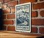 A sign for Rapid City, South Dakota, featuring a mountain landscape and a cityscape.