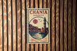A vintage-style poster of Chania, Greece, featuring a lighthouse and a cityscape, is displayed on a wooden wall.