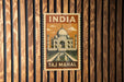 A vintage-style poster of the Taj Mahal, a famous mausoleum in India, is displayed on a wooden wall.