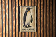 A framed image of a penguin is displayed on a wooden wall.
