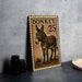 A metal sign featuring a donkey illustration and the number 25, placed on a countertop next to some black camera lenses.