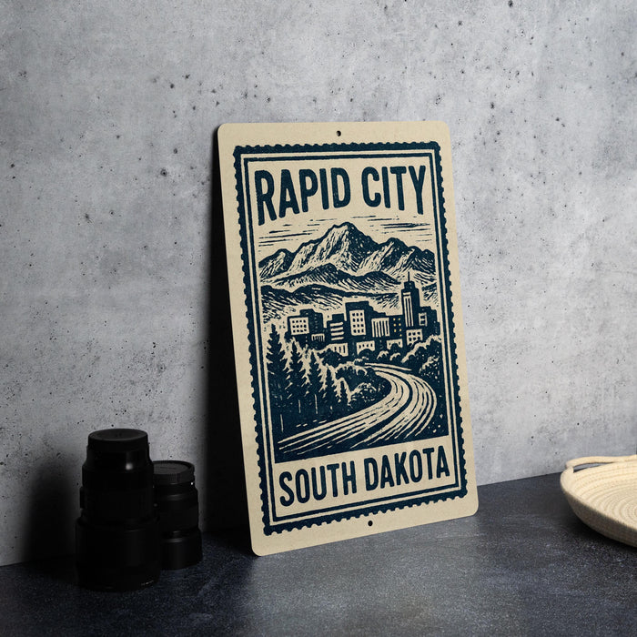 a sign for Rapid City, South Dakota, with a mountain landscape and a winding road.