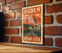 A vintage-style metal sign with the text "OGDEN" and "UTAH - USA" displayed on a brick wall.