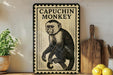 a framed illustration of a capuchin monkey on a shelf, with a potted plant to the left and a wooden cutting board to the right.