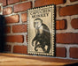 A framed illustration of a capuchin monkey is displayed on a brick wall.