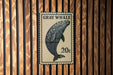 A postage stamp featuring a gray whale is displayed on a wooden wall.